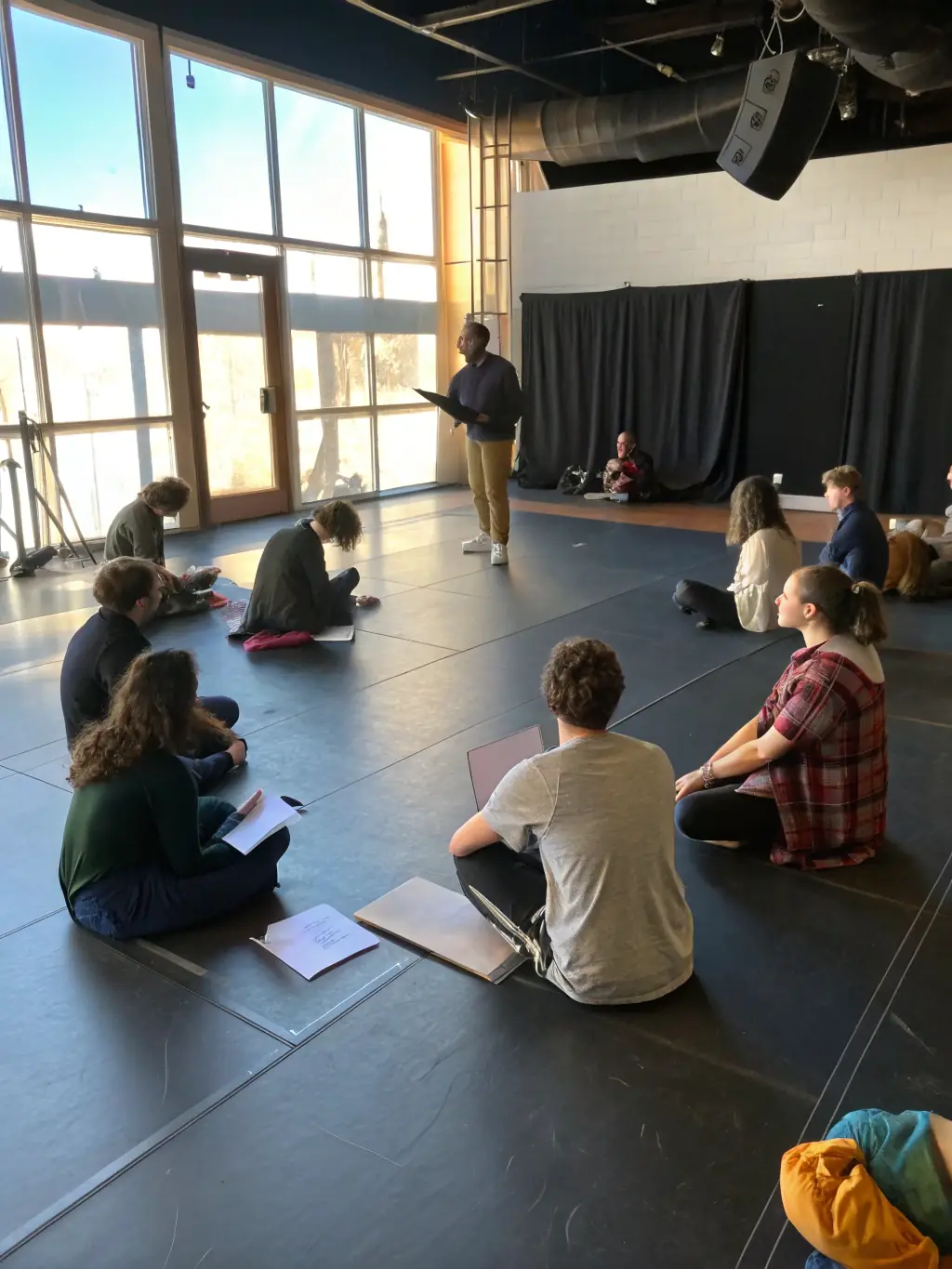 A group of diverse individuals participating in a theater workshop, focused on acting techniques and character development, organized by TAC'ON'ART.
